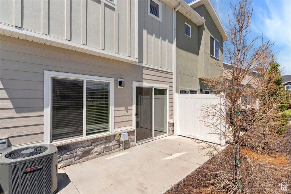 Rear view of house featuring central AC unit, a patio area, board and batten siding, and stone siding