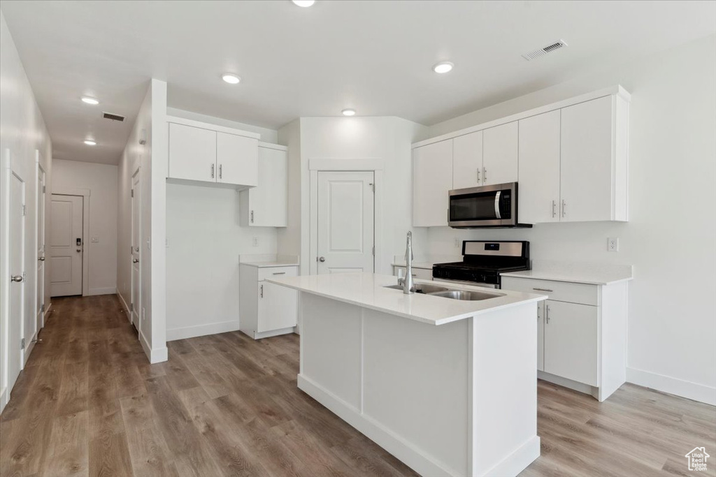 Kitchen with stainless steel appliances, light wood-style flooring, a sink, baseboards, and white cabinetry