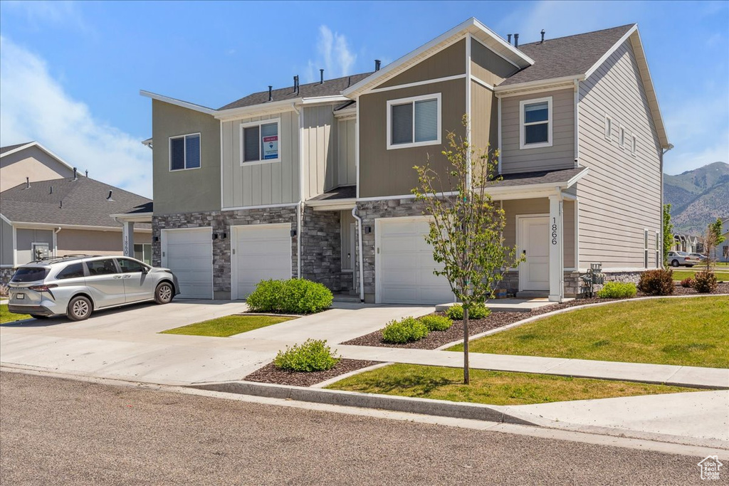 Multi unit property featuring a garage, stone siding, driveway, and a front yard