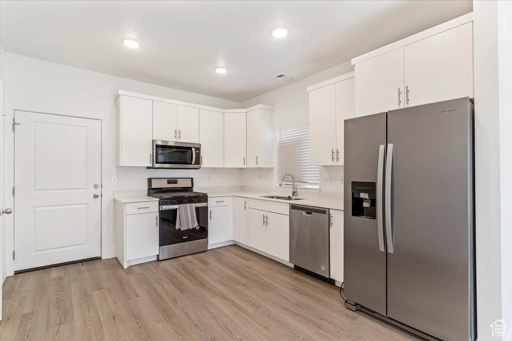 Kitchen featuring stainless steel appliances, a sink, light countertops, white cabinets, and light wood-style floors