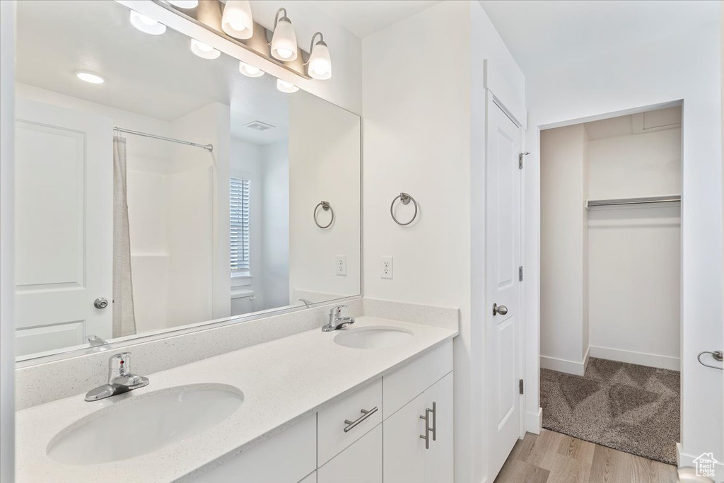 Full bath featuring double vanity, wood finished floors, a shower, and baseboards