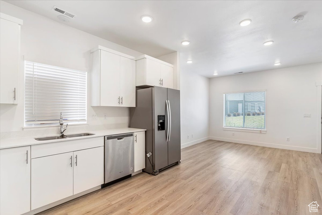 Kitchen with appliances with stainless steel finishes, a sink, light wood finished floors, white cabinets, and recessed lighting