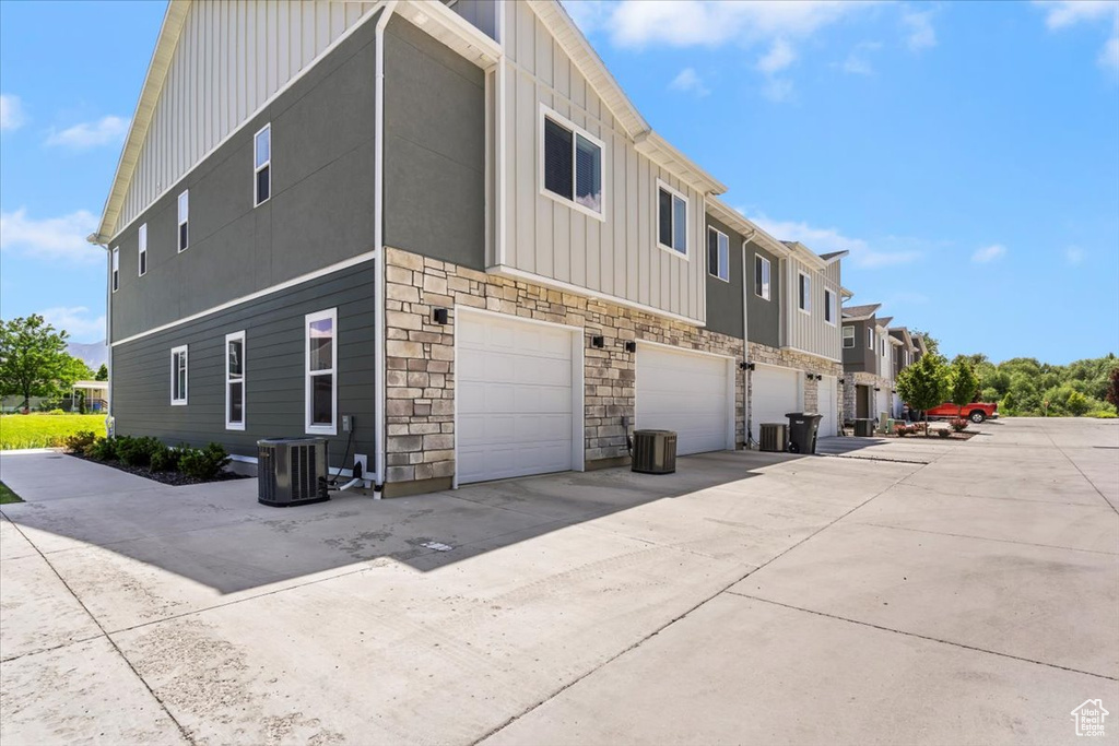 View of side of home featuring board and batten siding, stone siding, a garage, central AC unit, and a residential view