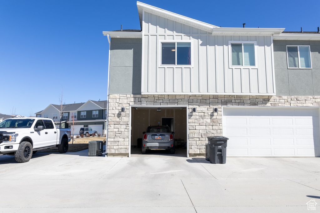 View of home\'s exterior with board and batten siding, stone siding, cooling unit, and an attached garage