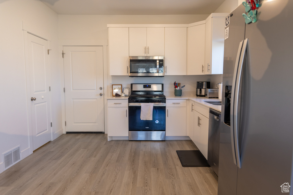 Kitchen with stainless steel appliances, light wood-type flooring, light countertops, and white cabinets