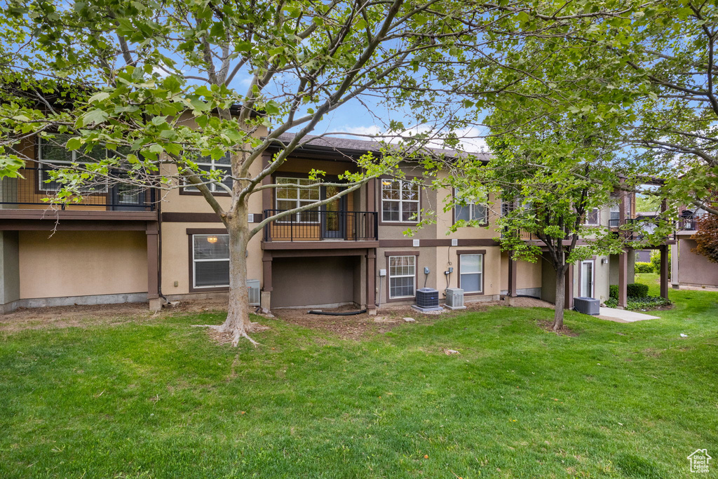 Back of house featuring stucco siding, a yard, central AC, and a balcony