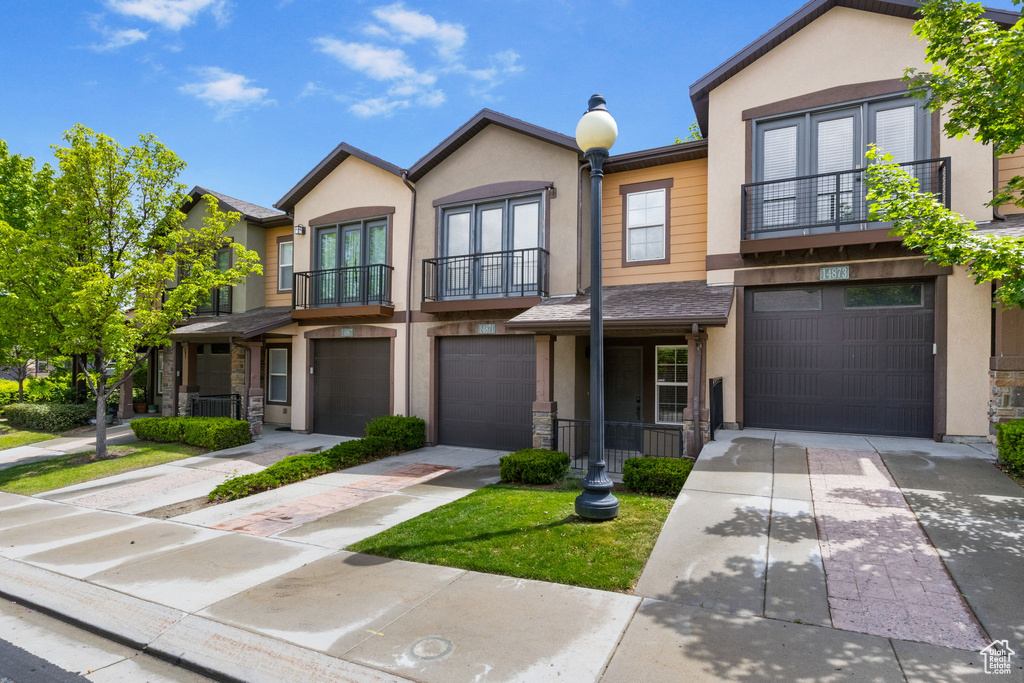 Townhome / multi-family property with a balcony, driveway, an attached garage, and stucco siding