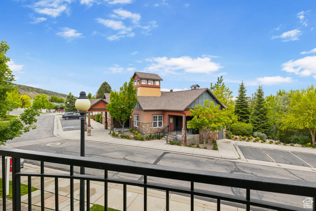 View of front of property with stone siding, a balcony, a chimney, and a shingled roof