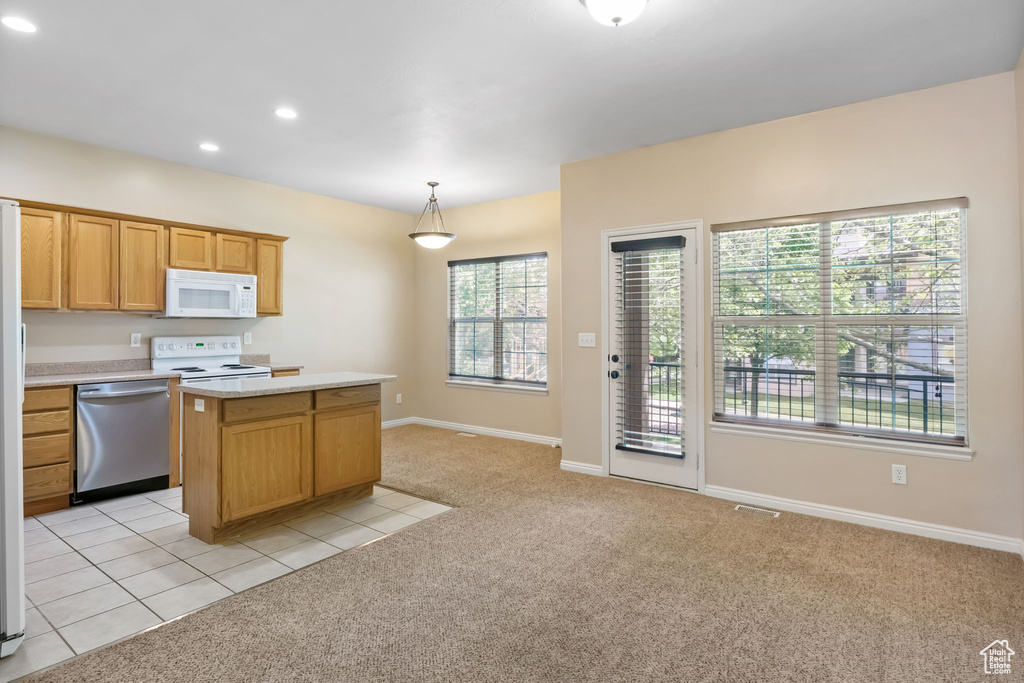 Kitchen featuring white appliances, light carpet, a kitchen island, light countertops, and baseboards
