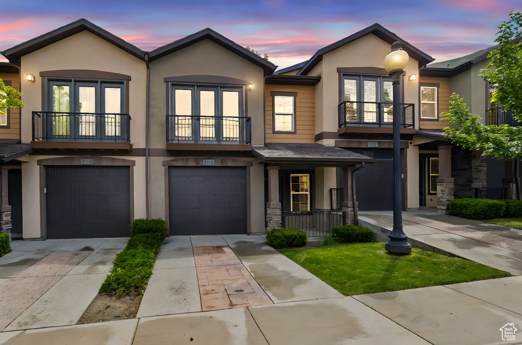 View of property featuring a balcony, french doors, stucco siding, a garage, and driveway