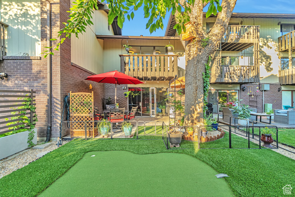 Back of house with a putting area, brick siding, a balcony, and a patio area