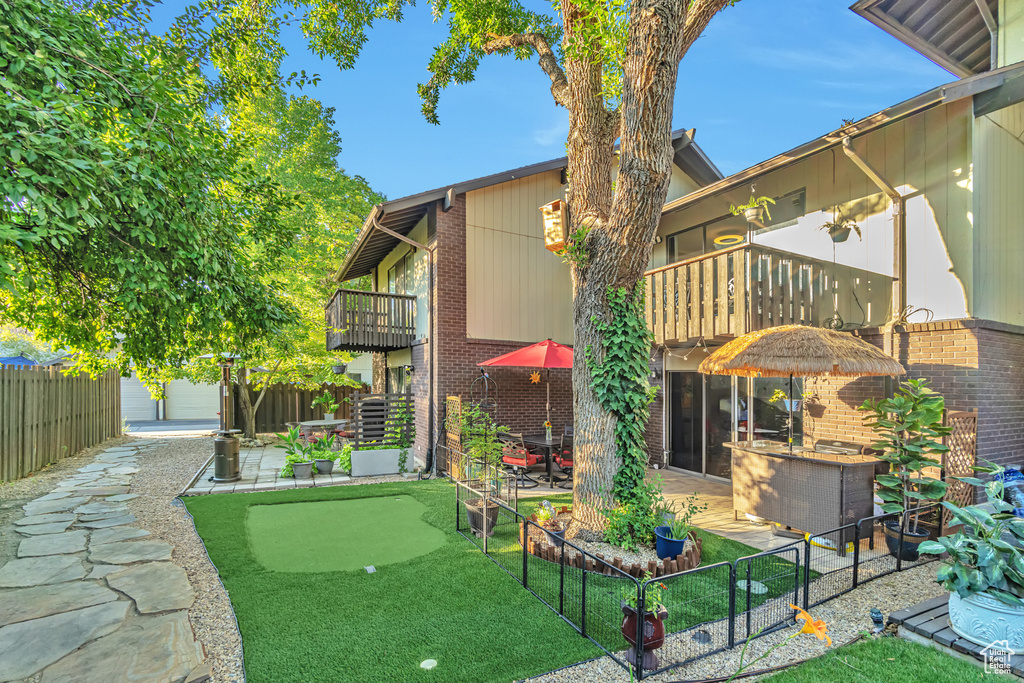 Back of house featuring a balcony, a putting area, a patio area, and brick siding