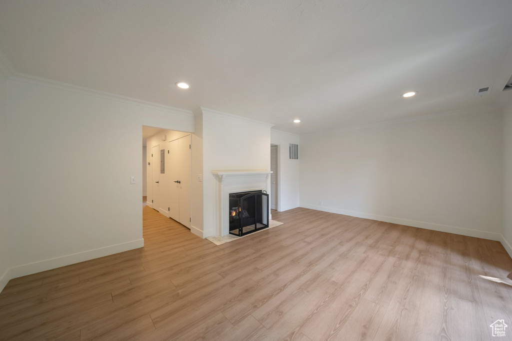Unfurnished living room featuring recessed lighting, baseboards, light wood-style flooring, ornamental molding, and a fireplace with flush hearth