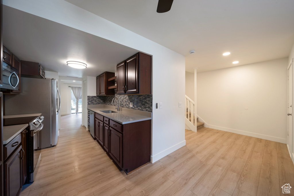 Kitchen featuring stainless steel appliances, a sink, dark brown cabinets, light wood finished floors, and light countertops