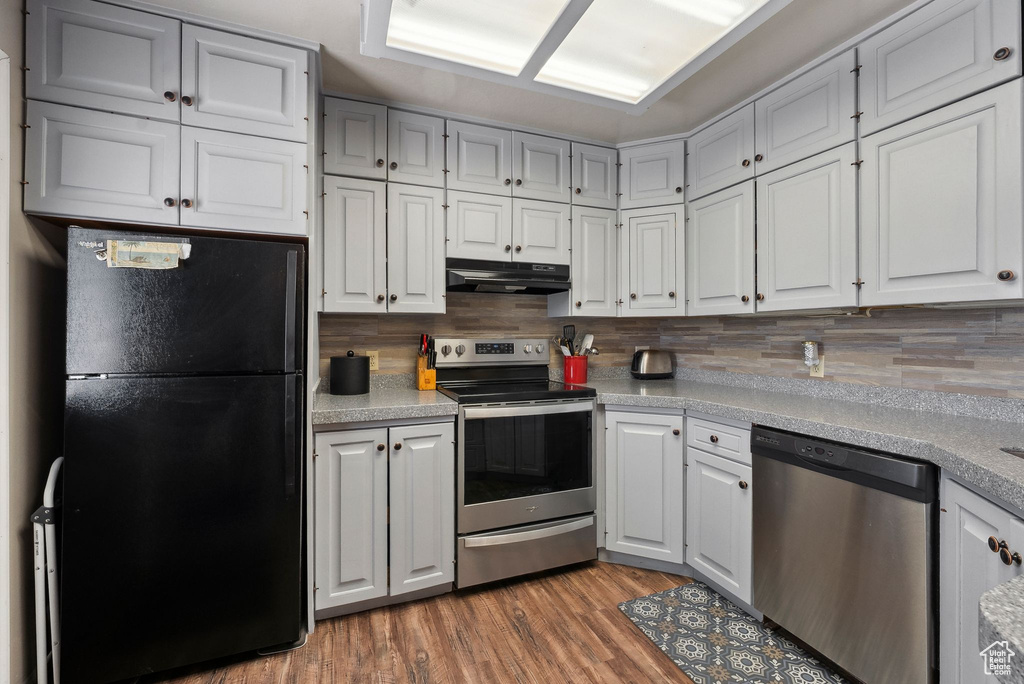 Kitchen with appliances with stainless steel finishes, under cabinet range hood, tasteful backsplash, light countertops, and light wood finished floors