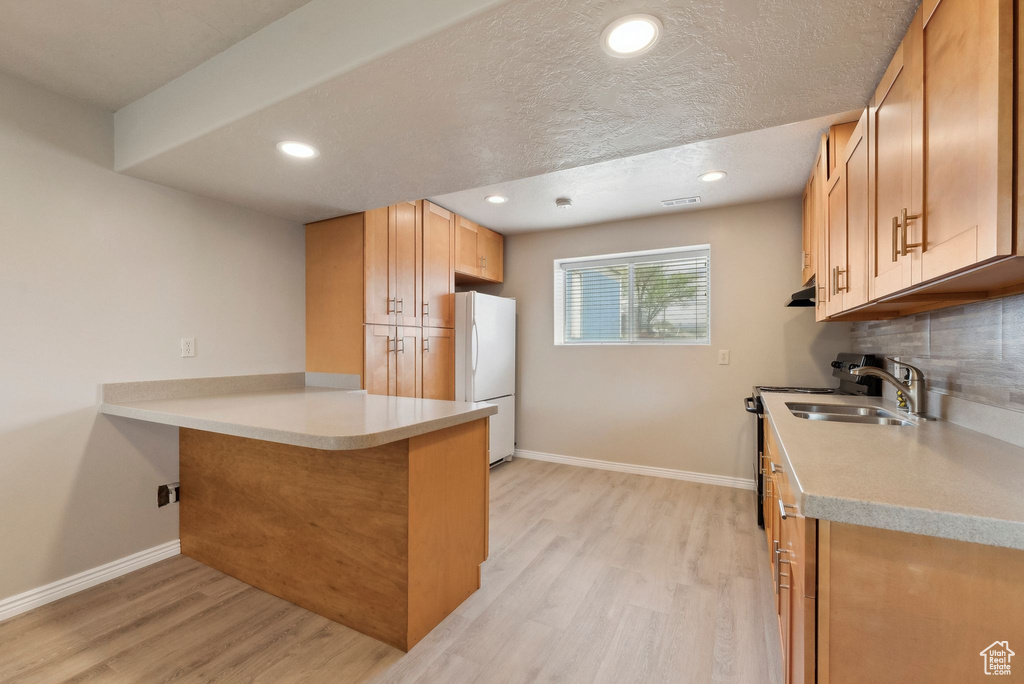 Kitchen featuring freestanding refrigerator, light wood-type flooring, baseboards, a peninsula, and a sink
