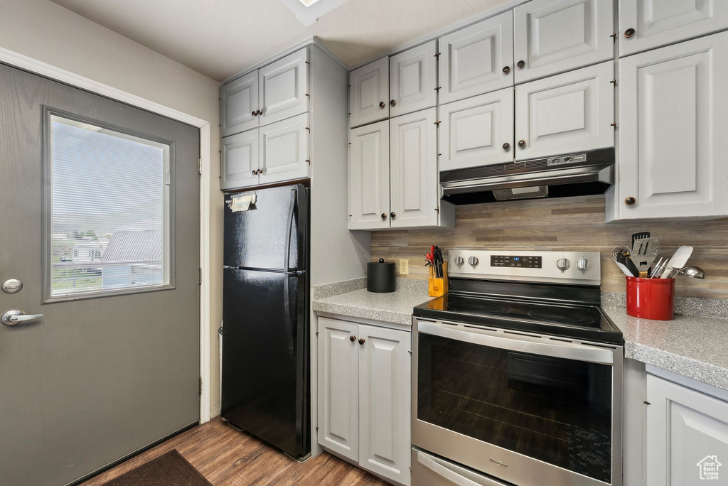 Kitchen with freestanding refrigerator, stainless steel range with electric cooktop, under cabinet range hood, light countertops, and backsplash