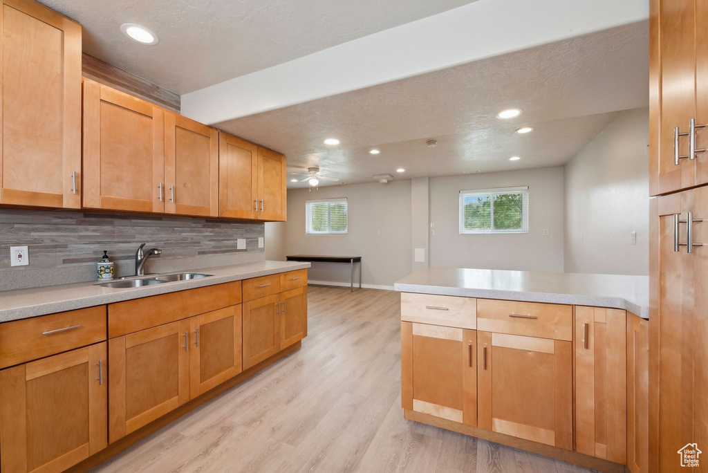 Kitchen with a sink, decorative backsplash, a peninsula, light wood finished floors, and healthy amount of natural light