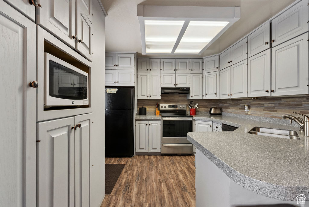 Kitchen featuring stainless steel electric range oven, freestanding refrigerator, under cabinet range hood, a sink, and backsplash