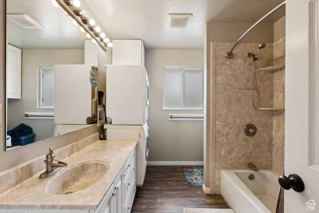 Full bathroom featuring stacked washer and clothes dryer, wood finished floors, shower / bath combination, vanity, and baseboards