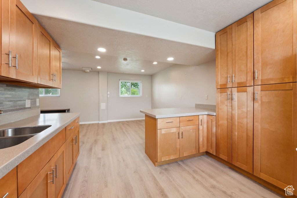 Kitchen featuring a peninsula, light wood-style floors, a sink, recessed lighting, and light countertops