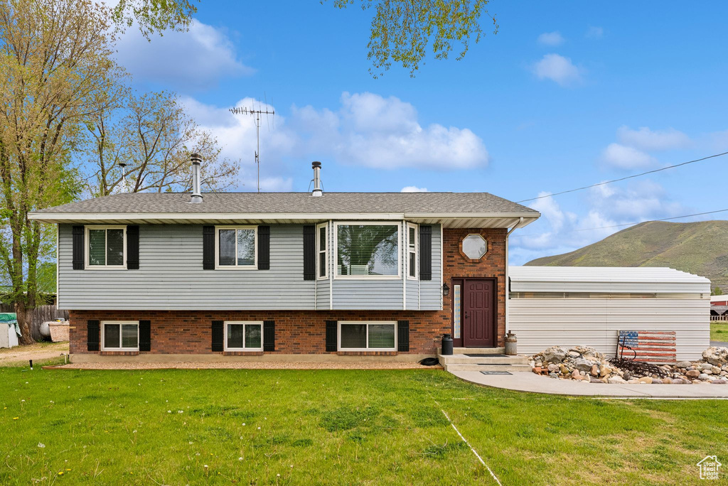Raised ranch with a front yard, brick siding, and roof with shingles