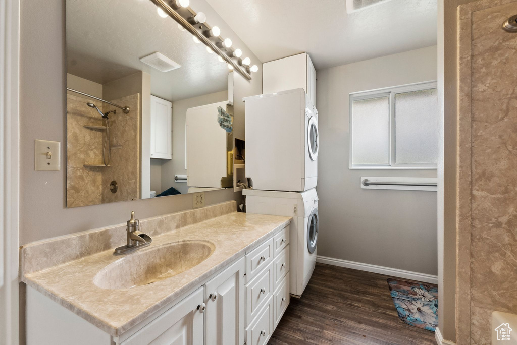 Bathroom featuring estacked washer and dryer, a shower, wood finished floors, baseboards, and vanity