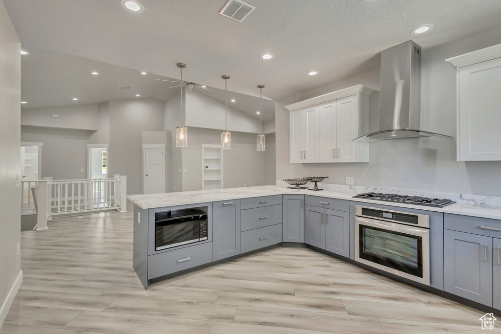 Kitchen with stainless steel appliances, wall chimney exhaust hood, gray cabinetry, a peninsula, and light wood-style flooring