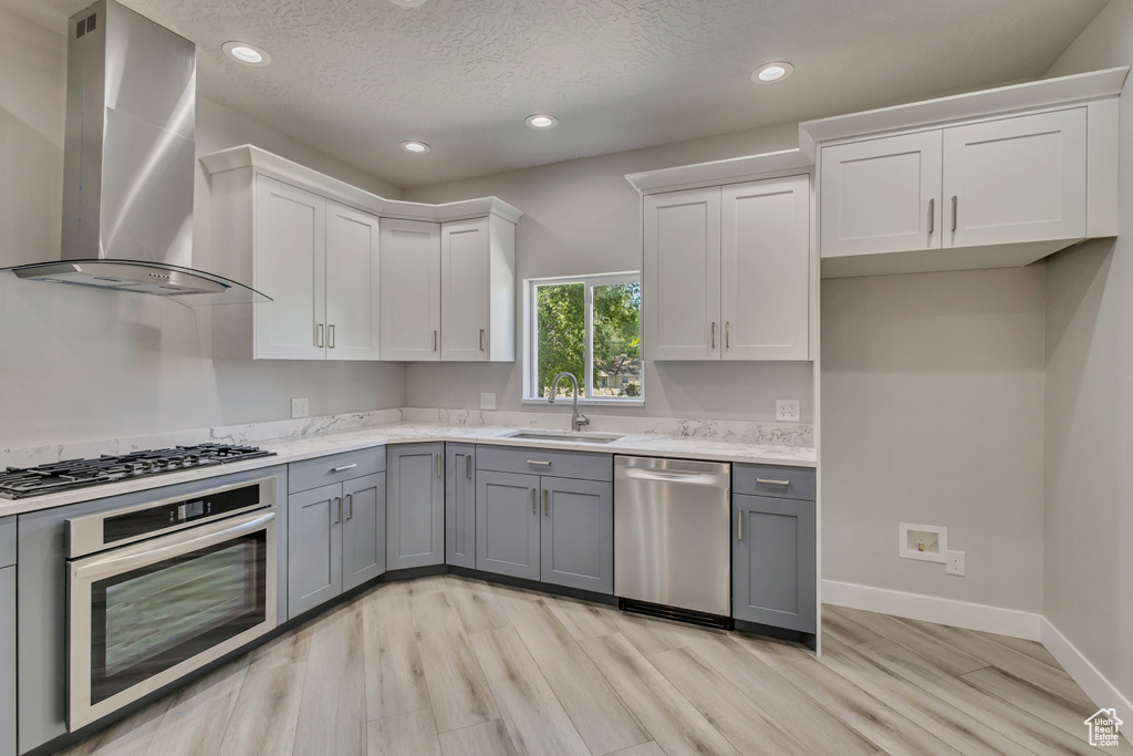 Kitchen featuring stainless steel appliances, a sink, wall chimney exhaust hood, gray cabinetry, and recessed lighting
