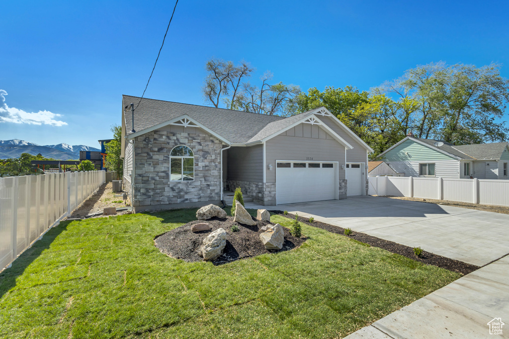 View of front of house featuring an attached garage, concrete driveway, stone siding, a mountain view, and a shingled roof