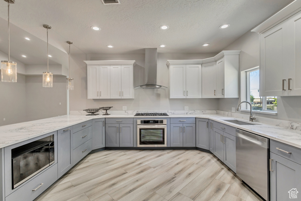 Kitchen featuring appliances with stainless steel finishes, wall chimney range hood, a sink, gray cabinetry, and recessed lighting