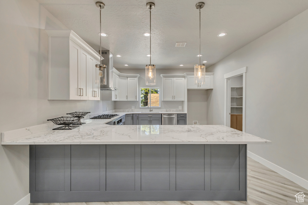Kitchen featuring a peninsula, baseboards, light stone countertops, wall chimney exhaust hood, and recessed lighting