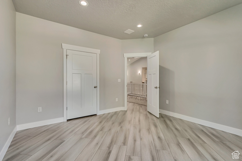 Unfurnished bedroom featuring light wood-type flooring, a textured ceiling, baseboards, and recessed lighting