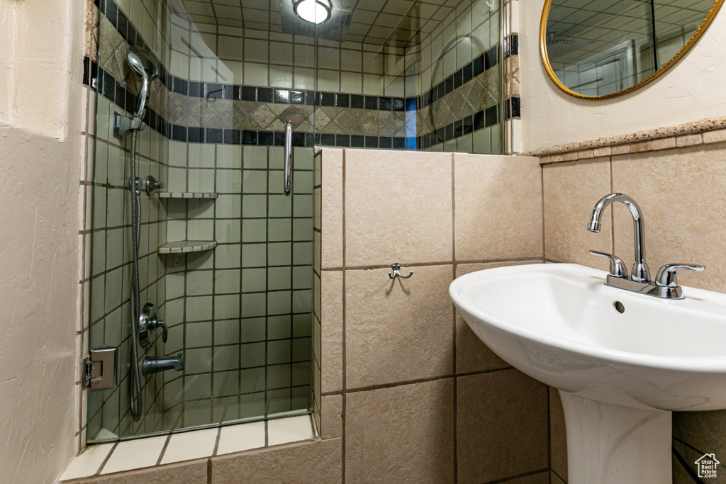 Full bath featuring a tile shower, tile walls, a sink, and a textured wall