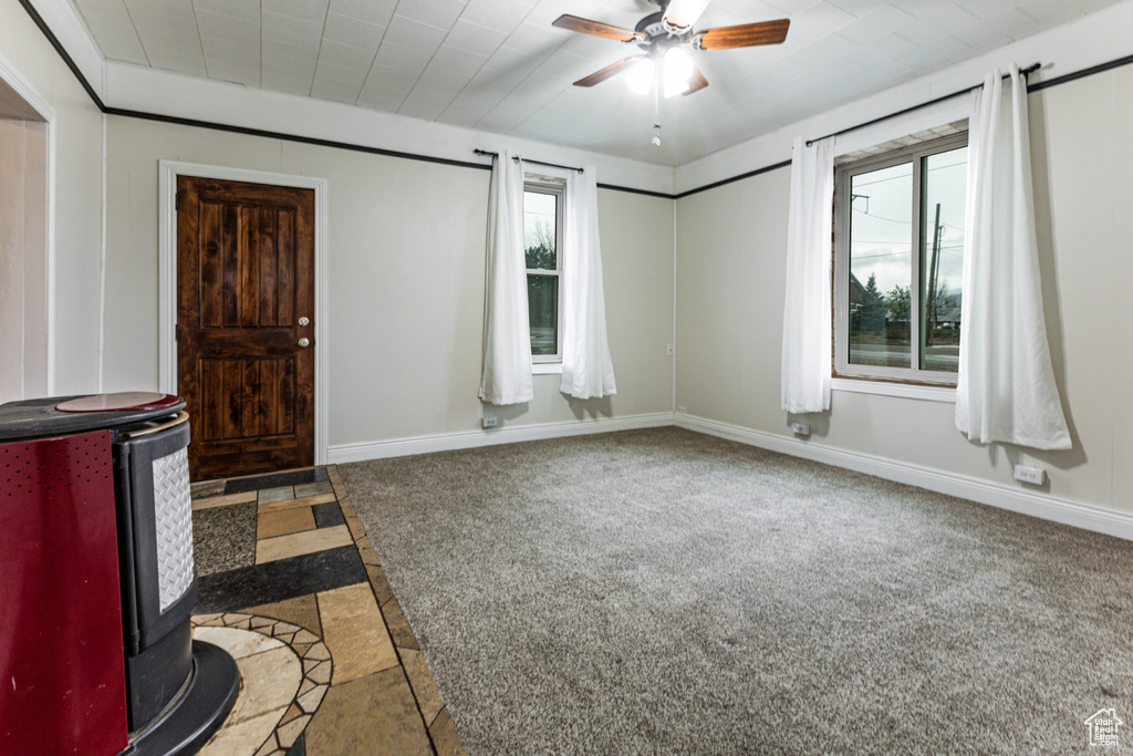 Empty room with a ceiling fan, plenty of natural light, a wood stove, and inlaid floor details