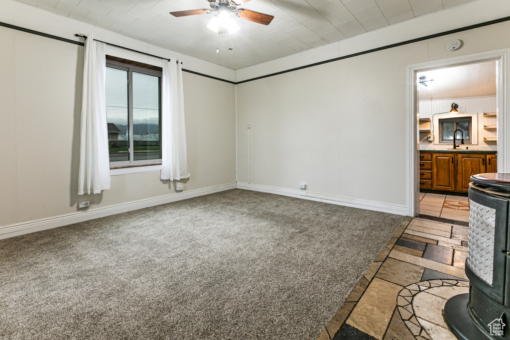 Empty room featuring ceiling fan, a sink, a wood stove, baseboards, and inlaid floor details