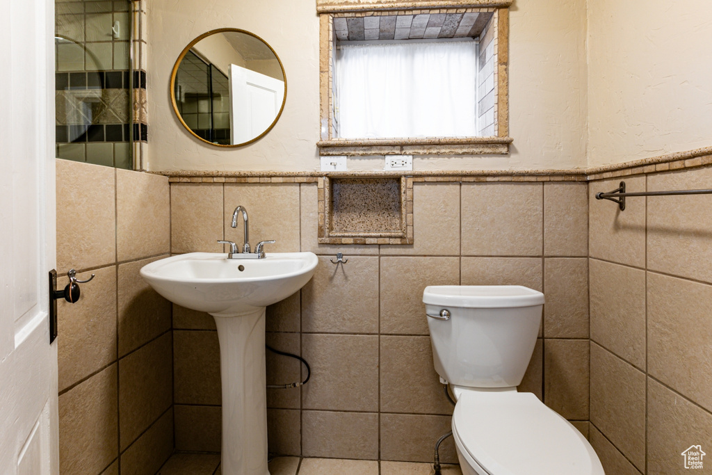 Bathroom with toilet, tile walls, a wainscoted wall, and a sink
