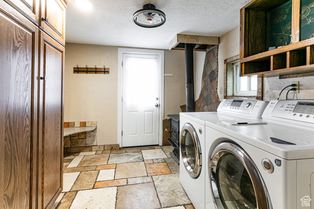 Laundry area with washer and clothes dryer, stone tile floors, cabinet space, and a wood stove