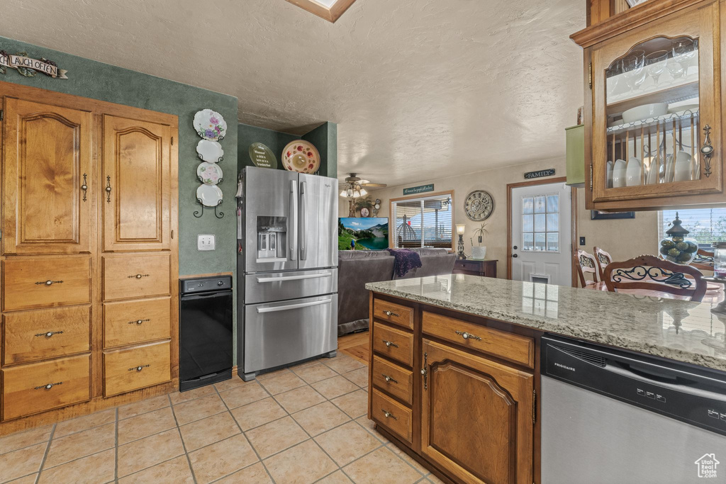 Kitchen featuring appliances with stainless steel finishes, healthy amount of natural light, light tile patterned floors, a textured ceiling, and brown cabinets