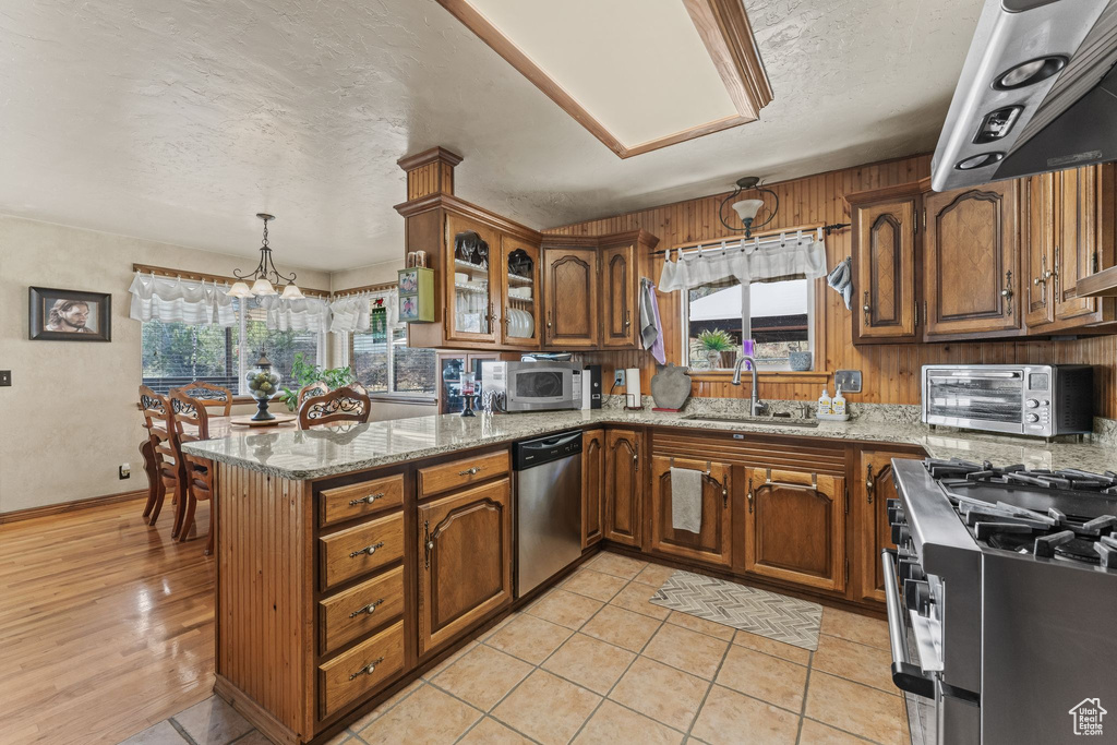 Kitchen featuring appliances with stainless steel finishes, a sink, brown cabinetry, a peninsula, and a textured ceiling