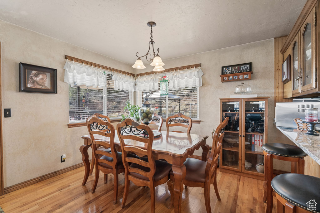 Dining area featuring light wood finished floors, baseboards, a textured wall, and a chandelier