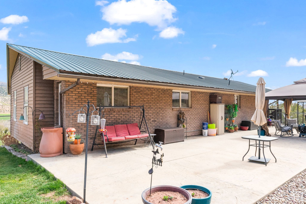 Back of property featuring a gazebo, a patio, brick siding, and metal roof