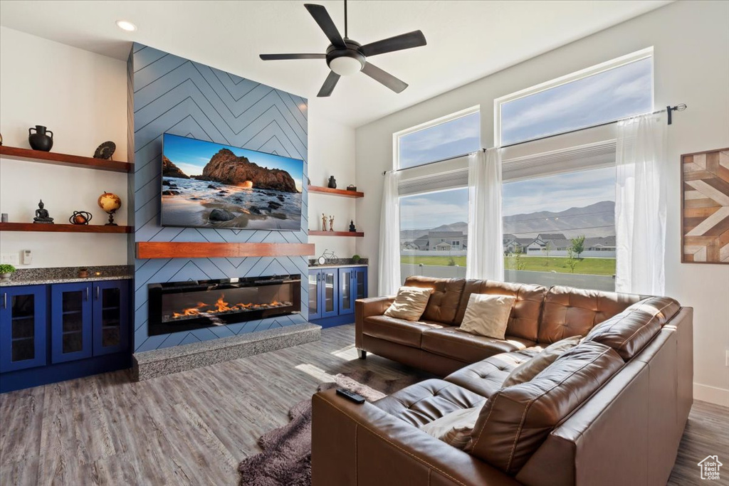 Living room with a ceiling fan, wood finished floors, a large fireplace, and baseboards