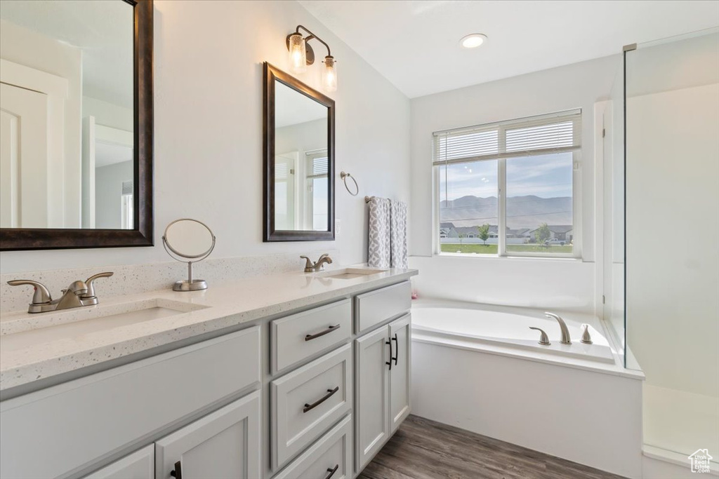 Bathroom featuring wood finished floors, double vanity, a garden tub, and recessed lighting