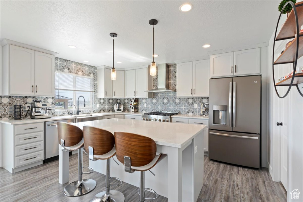 Kitchen with stainless steel appliances, wall chimney exhaust hood, decorative backsplash, light wood-style flooring, and recessed lighting