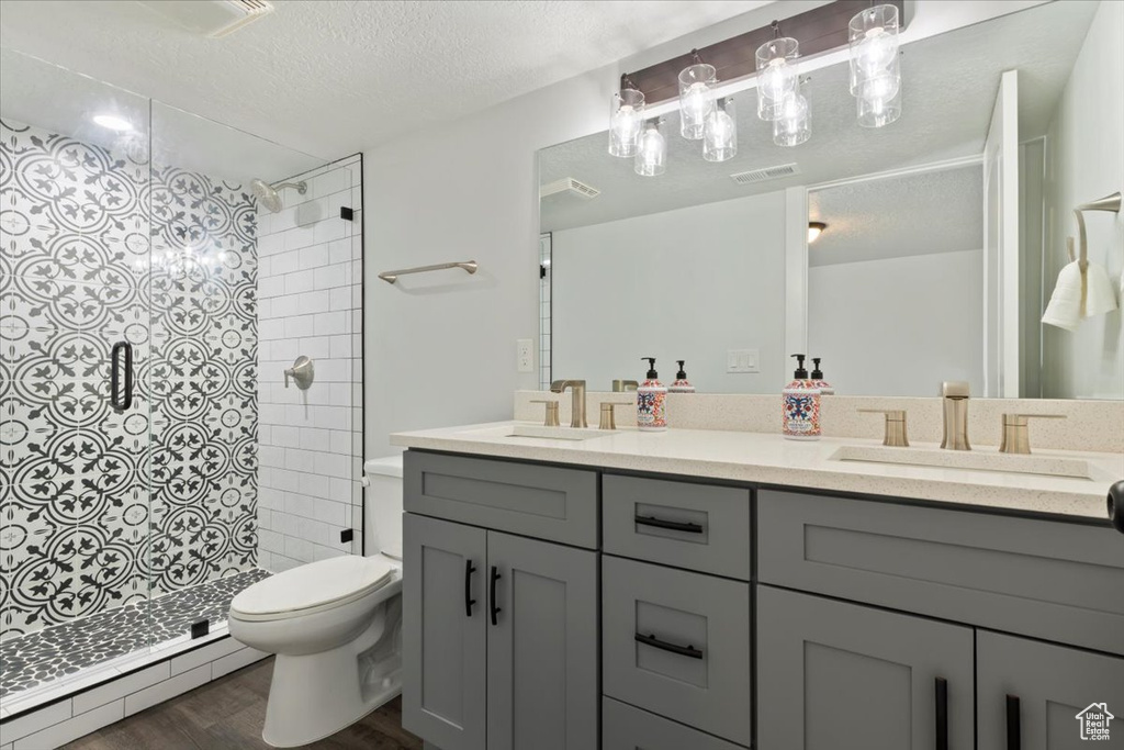Bathroom with a baseboard heating unit, toilet, a stall shower, double vanity, and a textured ceiling