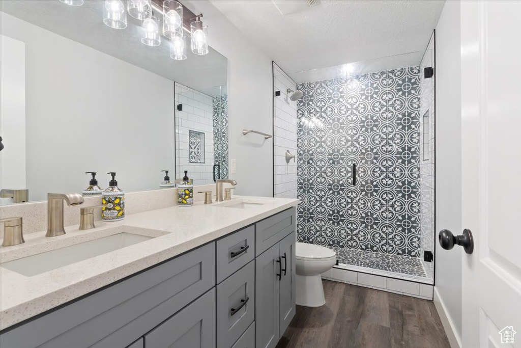 Bathroom featuring toilet, tiled shower, wood finished floors, and double vanity