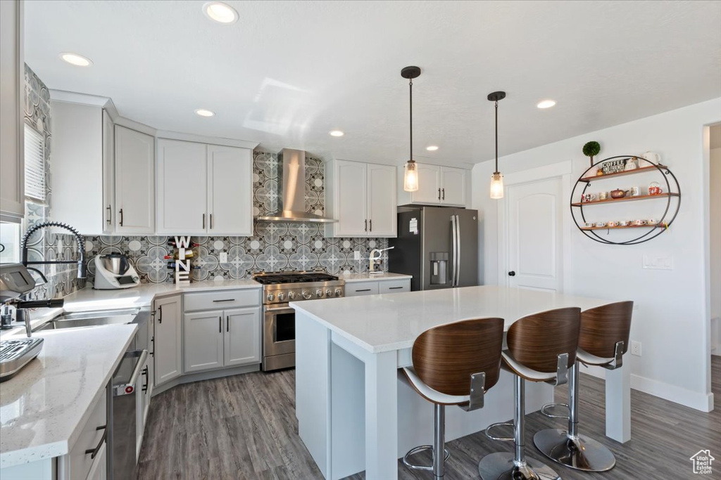 Kitchen featuring appliances with stainless steel finishes, wall chimney exhaust hood, dark wood finished floors, decorative backsplash, and a breakfast bar area