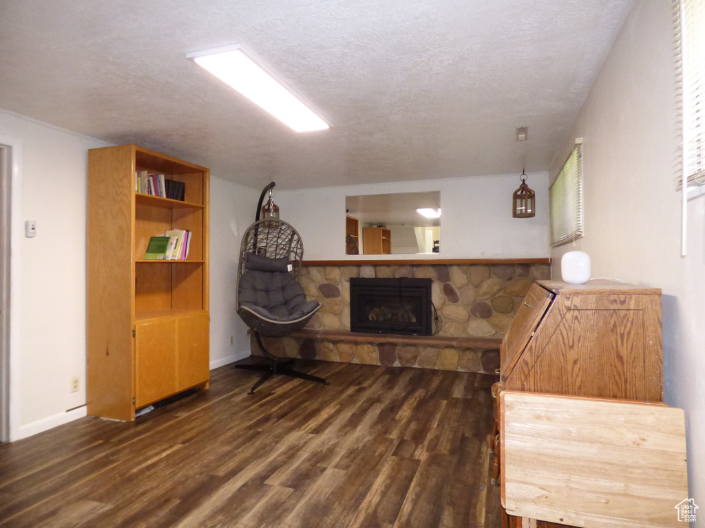 Below grade area with dark wood-style flooring, a stone fireplace, a textured ceiling, and baseboards