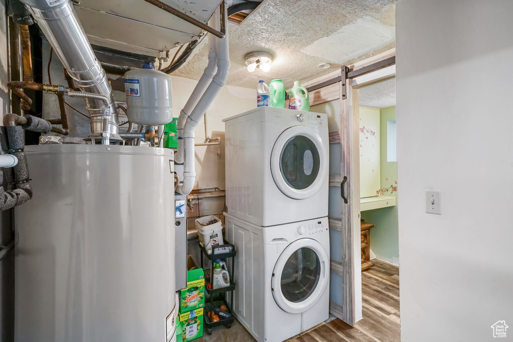 Laundry area with gas water heater, estacked washer and dryer, and wood finished floors